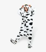 Adult wearing a black and white cow onesie playfully lifting one leg, front view.