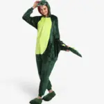 Woman smiling playfully and holding the tail while wearing the comfortable Dinosaur Onesie For Adults.